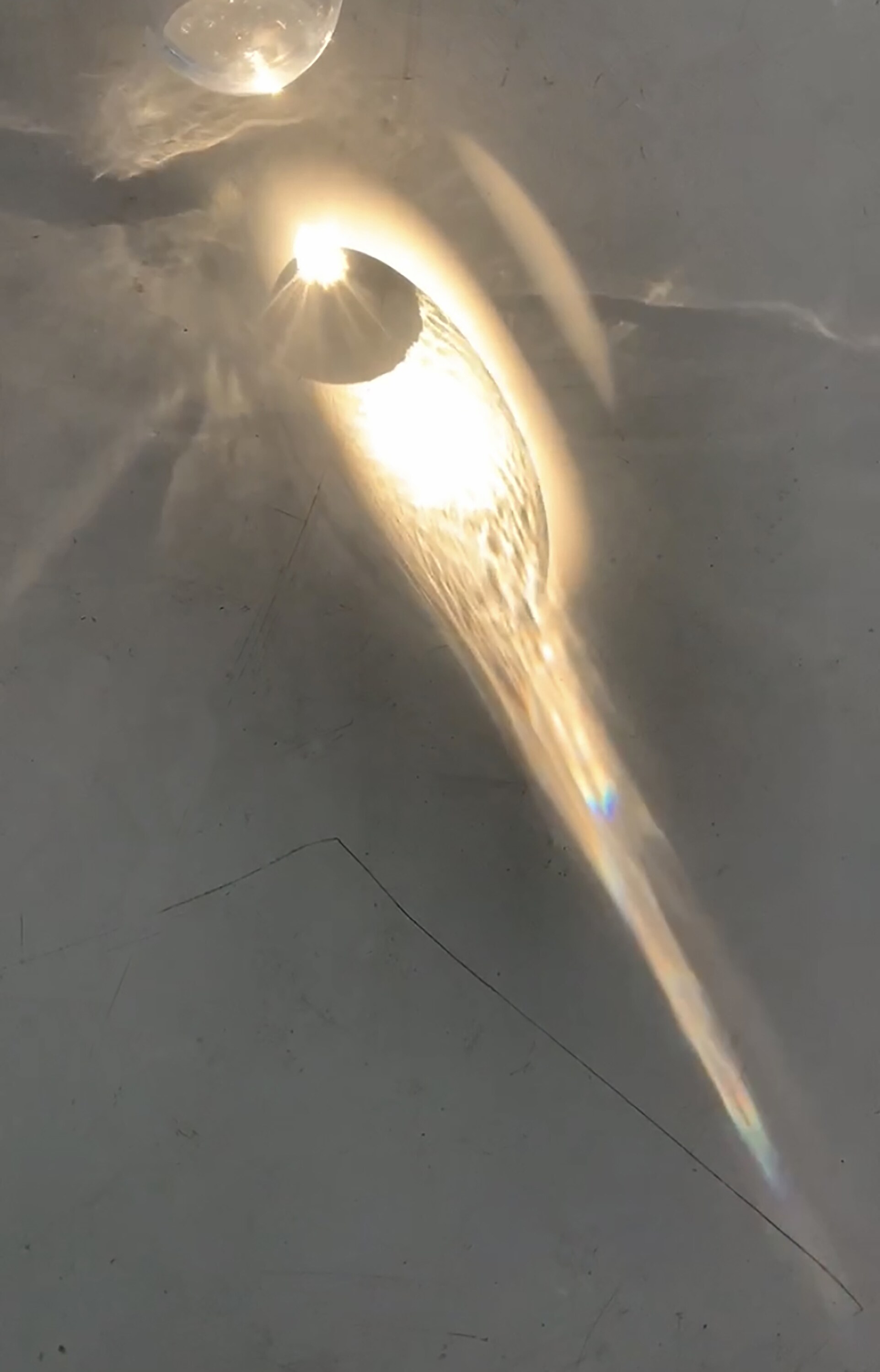 A warm arc of refracted natural light across a pale surface