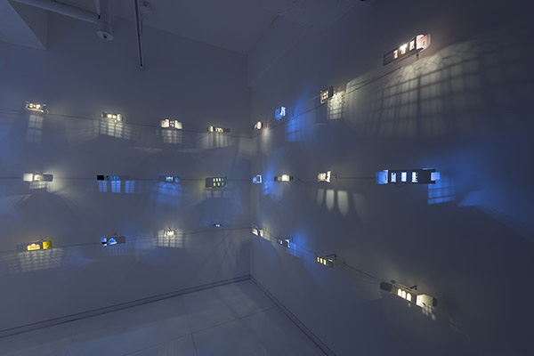 Darkened gallery installation with illuminated architectural forms and projected window-like shadows