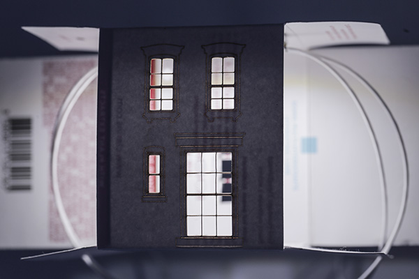 Close view of an illuminated house-like architectural form made with found packaging
