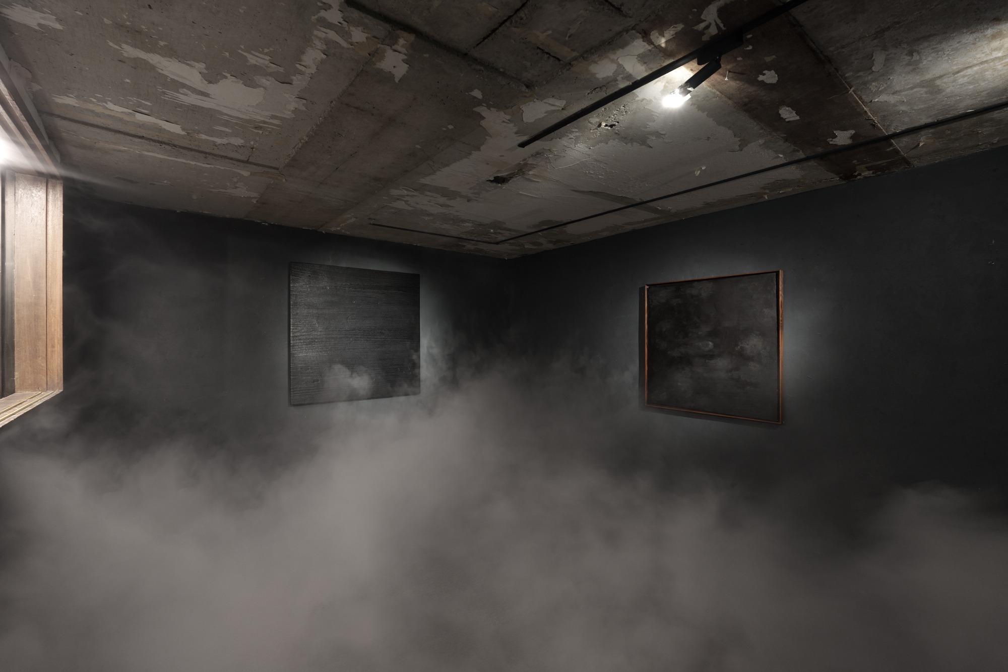 Two dark lacquer works installed in a black exhibition space with low fog