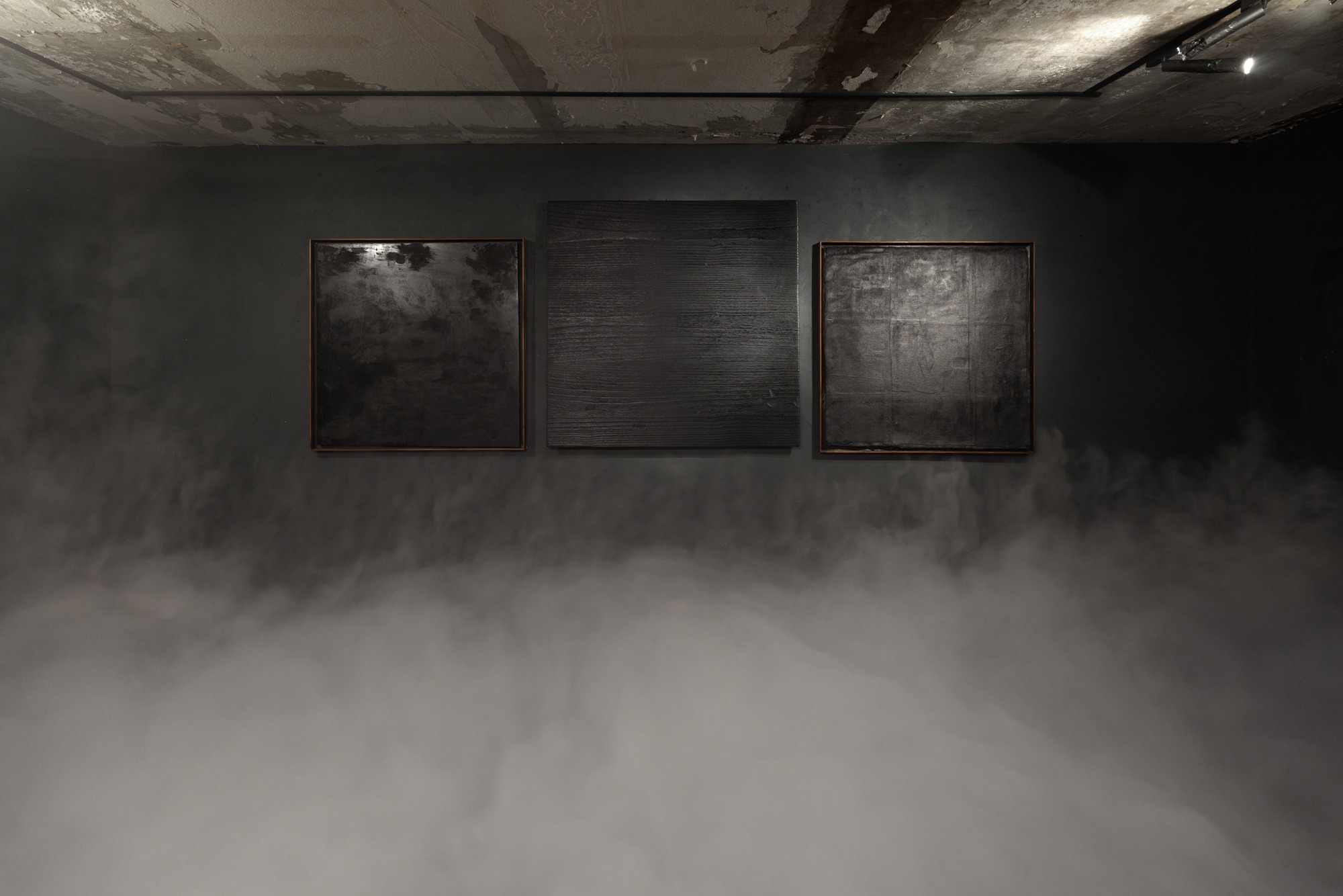 Three dark lacquer works installed together above low fog in an exhibition space